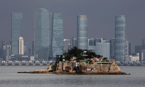 Photograph of a very small island with a few homes on it against a background of Xiamen's skyscrapers