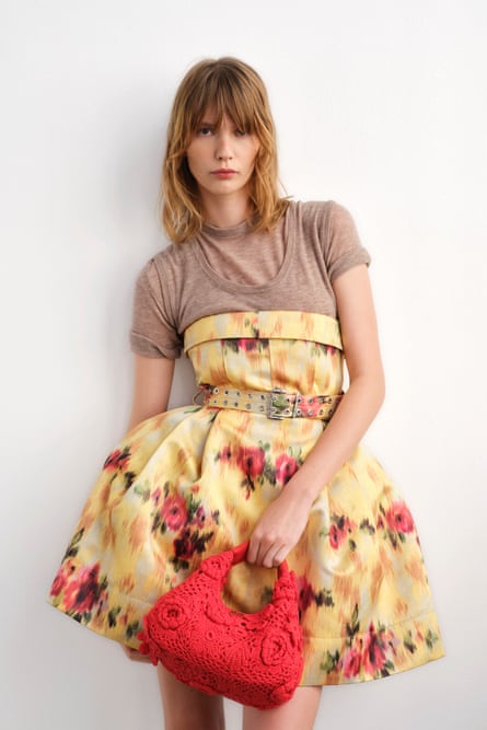 A model wearing a floral short dress, carrying a red handbag