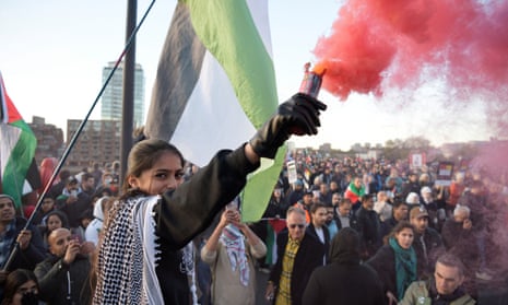 A girl wearing a keffiyeh holds a red flare on the march in London.