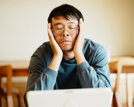 A stressed Asian man works on a laptop.