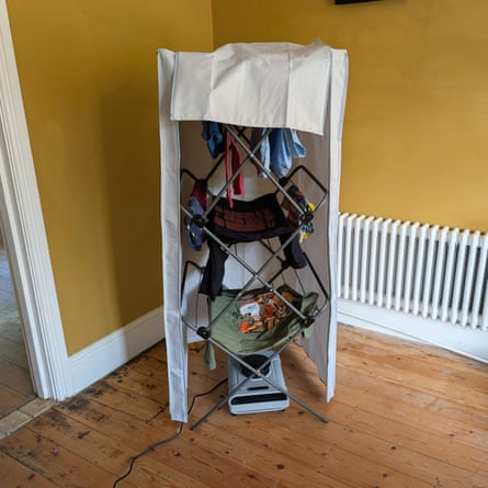A clothes airer covered with a heated drying pod, draped with laundry, stands beside a radiator
