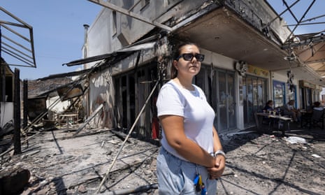 Pharmacy owner Anastasia Pissaka stands outside destroyed businesses that have been consumed by fire in Kiotari.