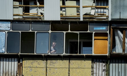 A man looks through the windows of his destroyed balcony.