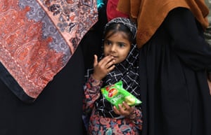 A young girl holds a packet of food as she stands among relatives