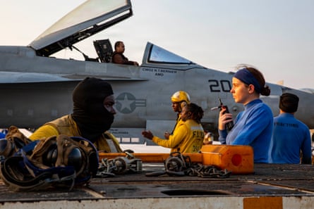 Crew members are in the foreground with the fighter jet behind. The pilot hatch is open with the pilot sitting inside