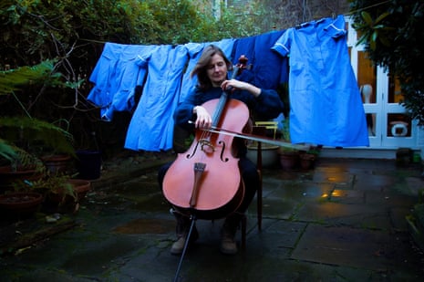 A nurse plays the cello in her garden in front of her uniform hanging on the washing line