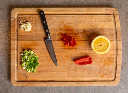 A cutting board with a red chilli pepper, scallion, garlic and lemon