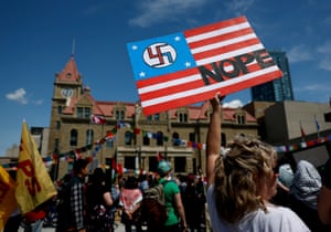 A demonstrator holds a sign with a swastika on the US flag with NOPE written over it