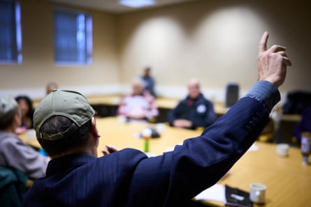 A person wearing a cap holds up his hand and wears a cap at a large table in a community centre