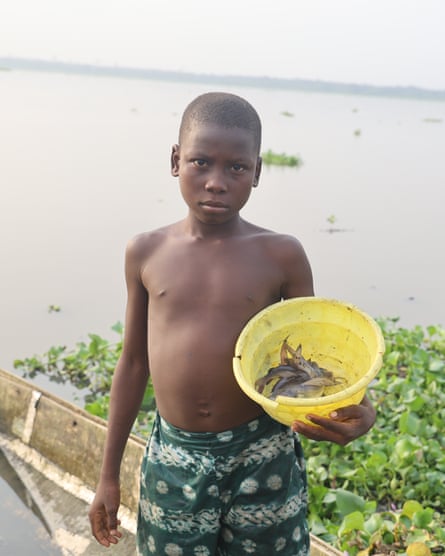 ‘The water is no longer our friend’: how dredging is pushing Lagos Lagoon towards ecosystem collapse – photo essay A boy holds a yellow bucket with a few fish in it.