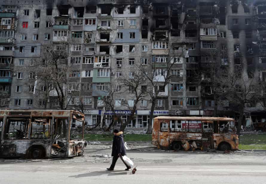 A local resident walks along a street past burnt out buses in Mariupol.