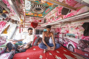 Two men sit inside the highly decorated pink interior of a truck