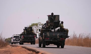 Troops sitting in the back of military vehicles as they drive along a road
