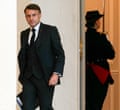 Emmanuel Macron, in a suit and lie, walks along holding a folder and looking confident