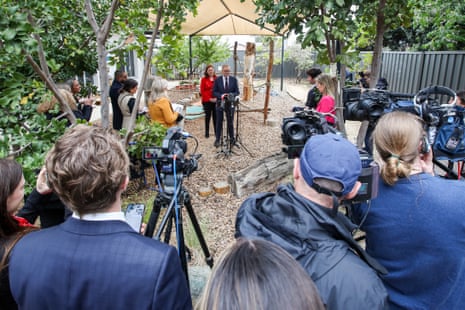 Anthony Albanese stands at a microphone and Louise Miller-Frost stands behind him in a playground, with a group of reporters and camera operators around them