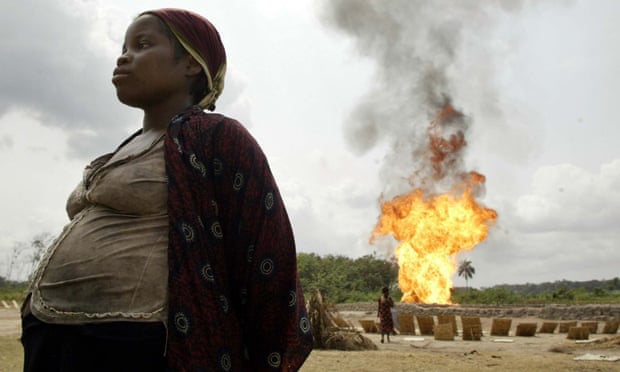 A gas flare is seen in the background as a pregnant woman dries tapioca near Utorogu flow station in Warri, Nigeria