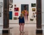 A woman stands looking at a painting in a gallery