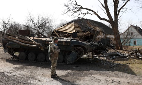 A Ukrainian soldier stands in front of a destroyed Russian armoured personnel carrier in Kyiv region