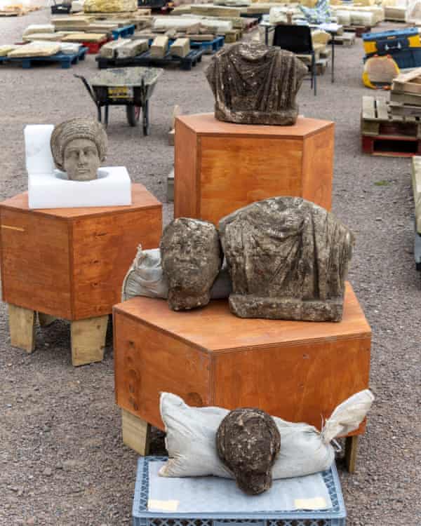 Three statue heads and two shoulders rest on display cases at the dig site.