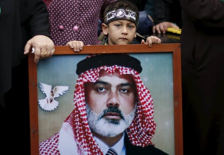 A boy stands behind a portrait of a man.