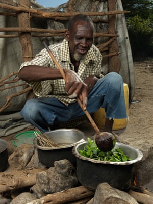 An old man stirs some green leaves into a cauldron