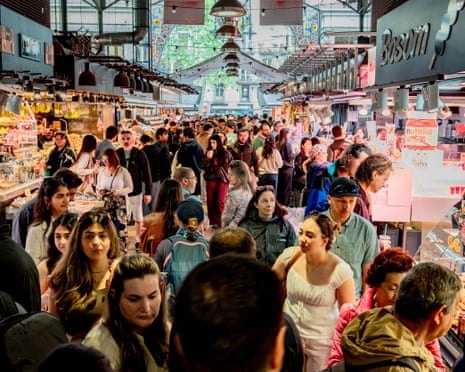A large crowd of people fills La Boqueria market hall with vendor stalls on both sides