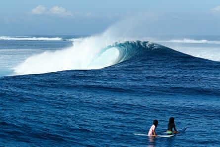 Two surfers riders sit on their boards and look at an empty wave at Cloudbreak.