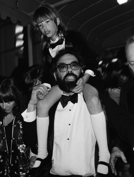 A black and white photograph of a man in a white shirt and bow tie. A young girl wearing a bow tie and a white shirt and white jacket is on his shoulders.