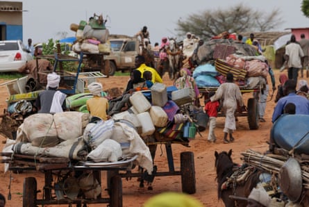 Sudanese people walk beside horse-drawn carts piled high with belongings at the Sudanese border with Chad