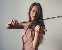 Geneva Lewis plays the violin, eyes closed, against a plain backdrop