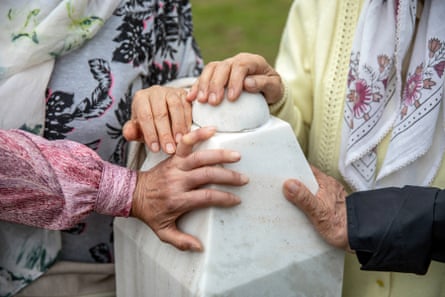 Four hands touch the top of one of the gravestones.