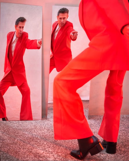 Willem Dafoe wears red suit with long jacket and flared trousers, white shirt and black boots, all by gucci.com.