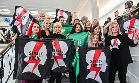 Women stand on the stairs in Poland's parliament holding flags.