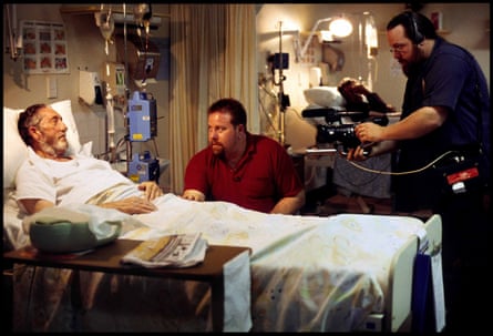 On-set still showing an older man in a hospital bed, with a younger man (Shane Jacobson) sitting beside him looking concerned, and Clayton Jacobson to the right with a camera rig, filming.