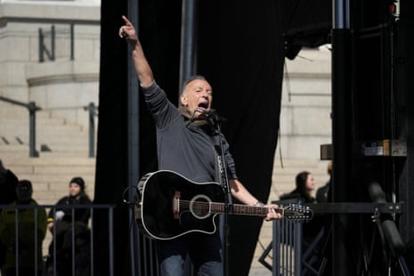 Bruce Springsteen raises arm while holding a guitar.