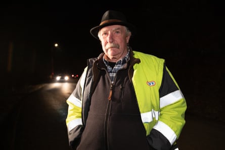 A man in hi-vis and a hat stands next to a road at night