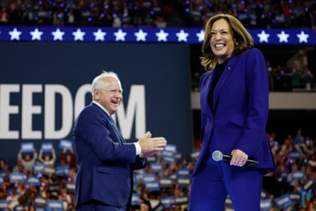a woman and a man smile on stage in an arena full of people