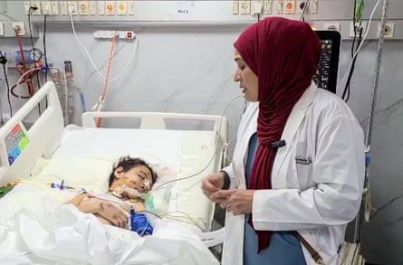 A doctor looks at a wounded child in a hospital bed