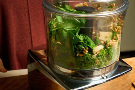 A food processor containing basil, pine nuts, cheese and garlic.