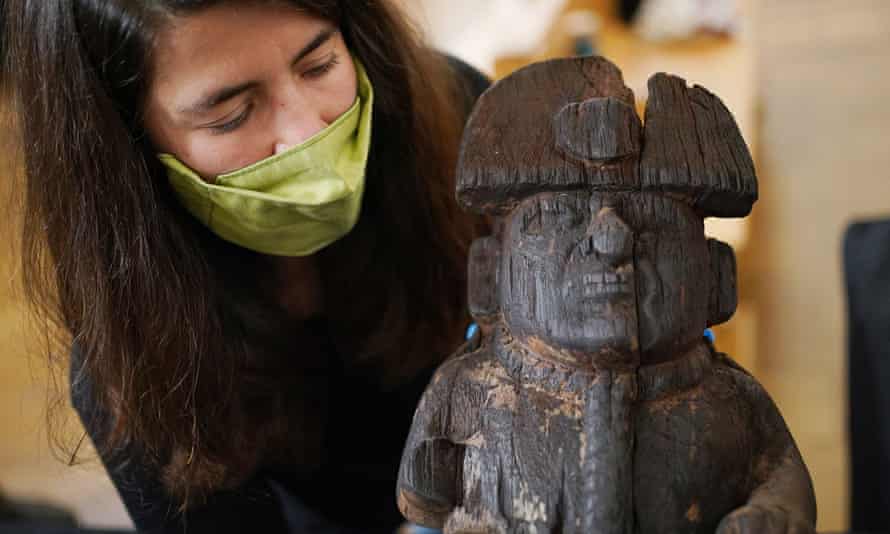 Collection manager Ana Carreira Galban holds a wooden figure depicting a bound prisoner with a headdress and rope around his neck, from the Moche people, dating AD100-800.
