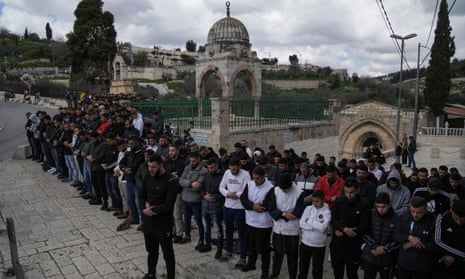 Dozens of Palestinian Muslim men stand in rows outside Jerusalem’s Old City with their heads bowed and pray. 