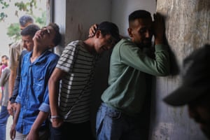 Men, clearly in distress and tearful, lean against a wall