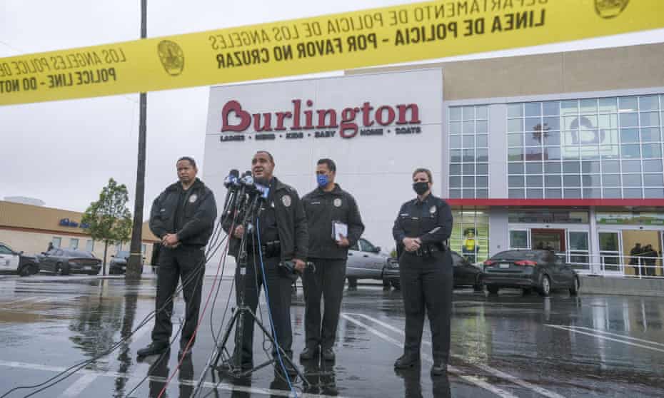 Four Los Angeles police officers stand in front of a cluster of microphones in the parking lot of a department store.