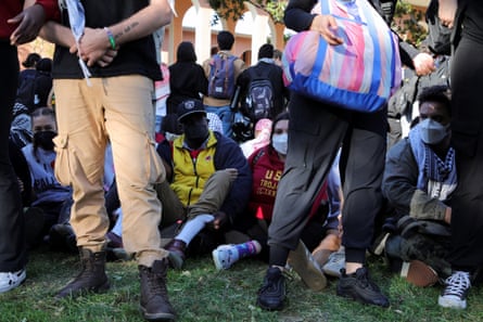 view of students seated on the ground behind other students’ legs
