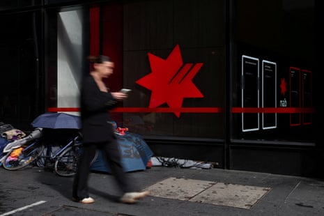 Blurred woman walking past an NAB building with a person’s belongings piled up by the wall