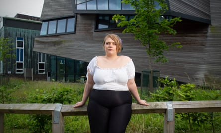 Emily Smith, in a short-sleeved shirt, props herself up against a wooden rail in front of a modern wooden building