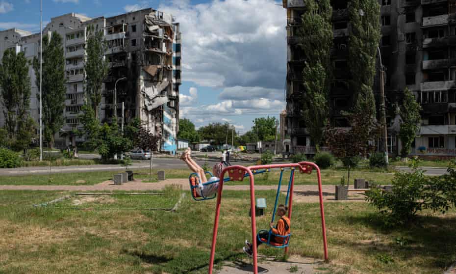 A girl and a boy swing on a swing next to a shelled apartment building in Borodianka, Ukraine.