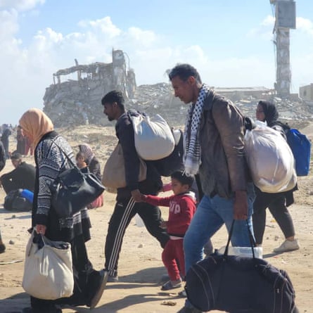 Crowds of people carry bags along a dusty path.