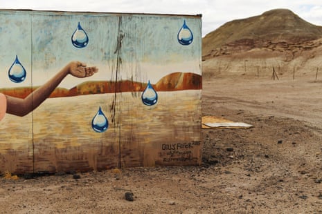 A mural on the side of a dirt road blends with the landscape. In the painting's dry landscape surrounded by mesas, a hand is extended to catch large drops of water falling from the sky.
