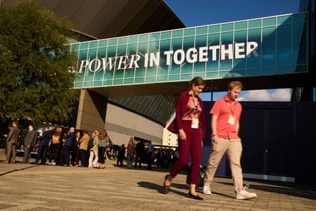 Two people with lanyards round their necks walk in front of the conference venue and a sign that reads: Power in together.